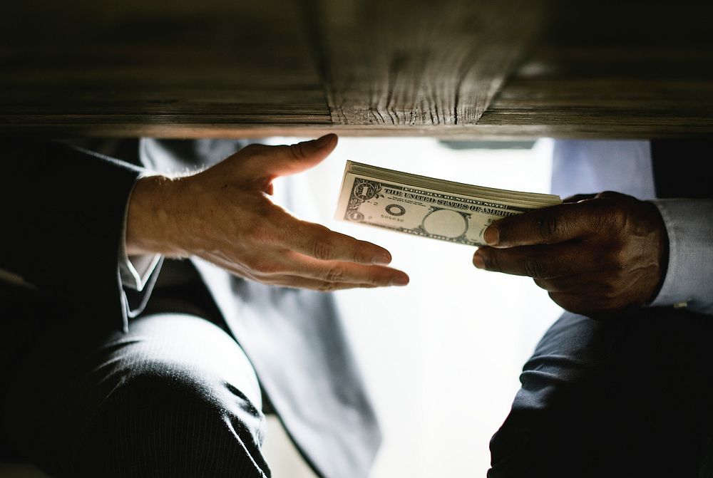 Hands passing money under table corruption bribery