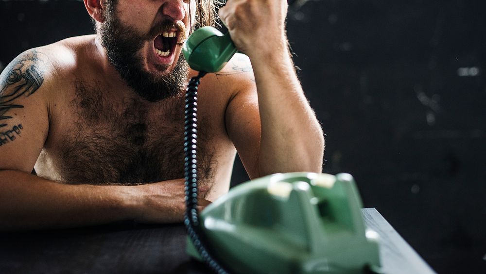 Caucasian topless man yelling over green vintage telephone