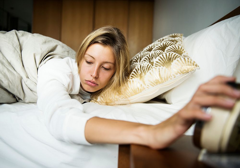 A sleepy Caucasian woman turning an alarm off