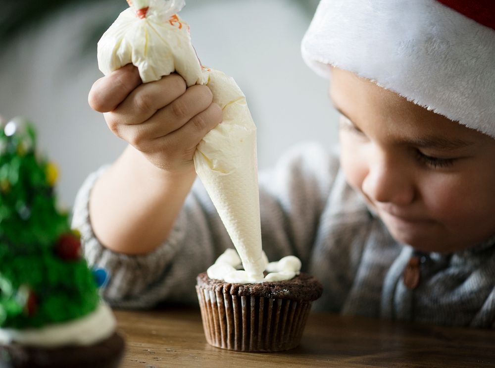 Little boy adding icing on a cupcake
