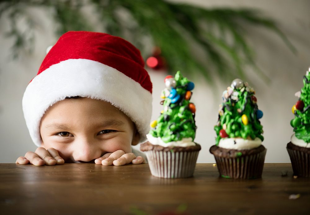 Cheerful little boy with Christmas tree decorated cupcakes