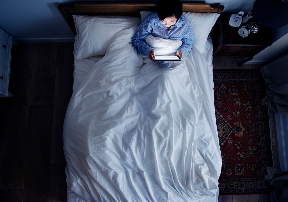 Woman in bed using a digital device in the dark