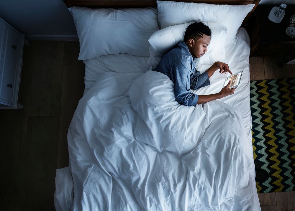 Man in bed using a digital device in the dark