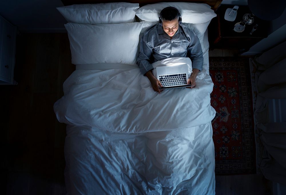 Man on bed using his laptop and a headphone