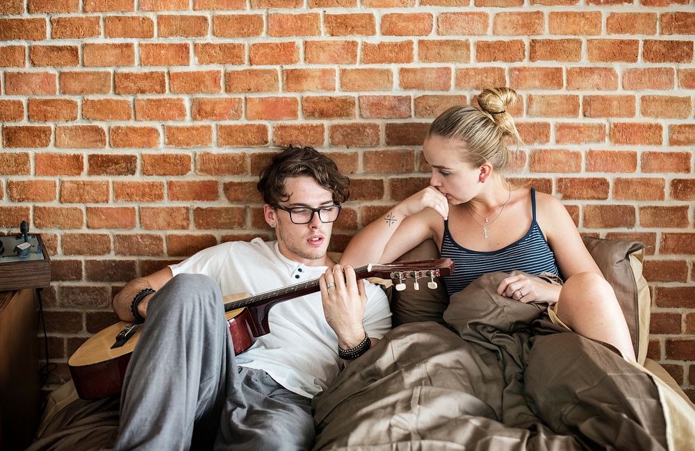 Caucasian couple on the bed, man playing a guitar