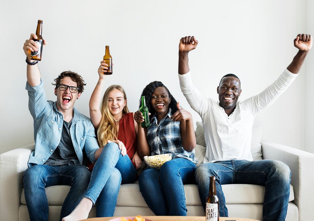 Group of diverse friends drinking and cheering while watching sports together