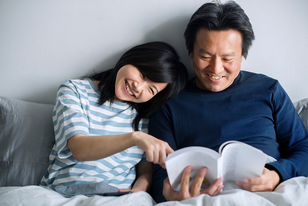 Asian couple reading a book on bed together