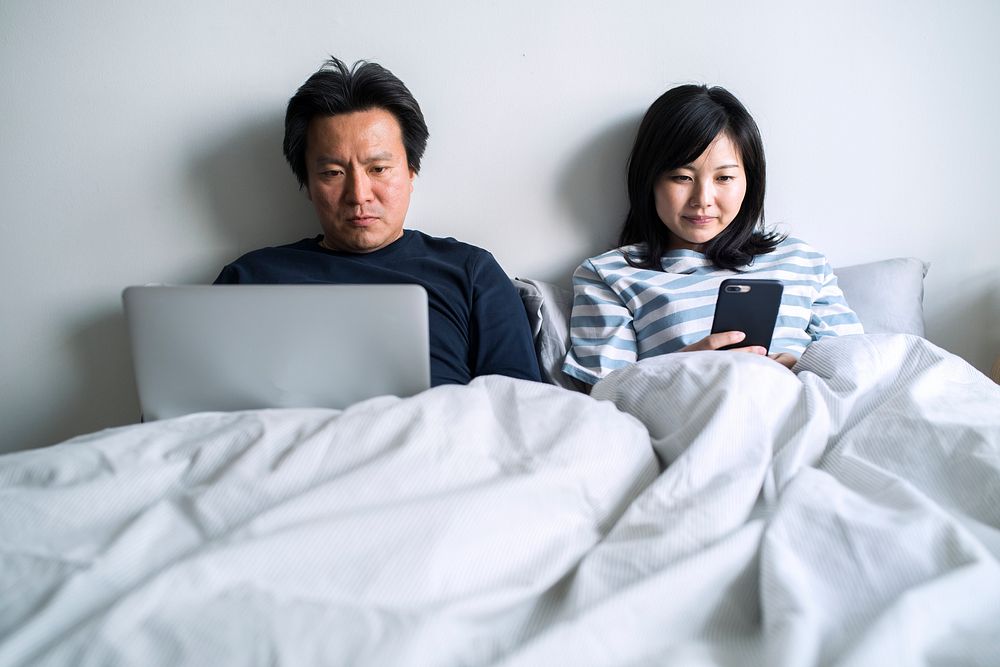 Asian couple using digital devices in bed