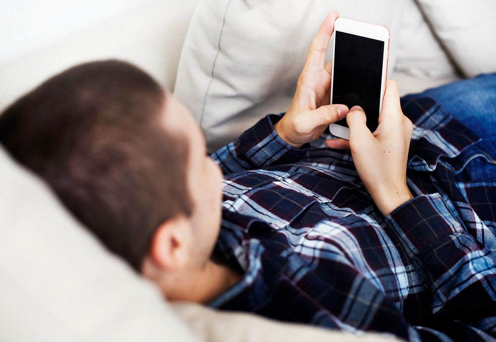 Man laid on the couch using a smartphone