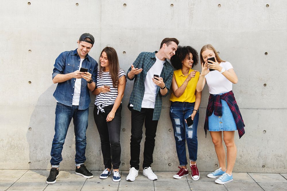 Group of young adults outdoors using smartphones together and chilling