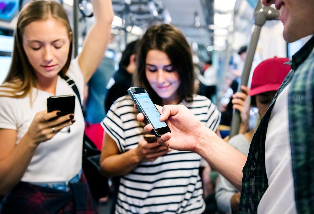 Group of young adult friends using smartphones in the subway