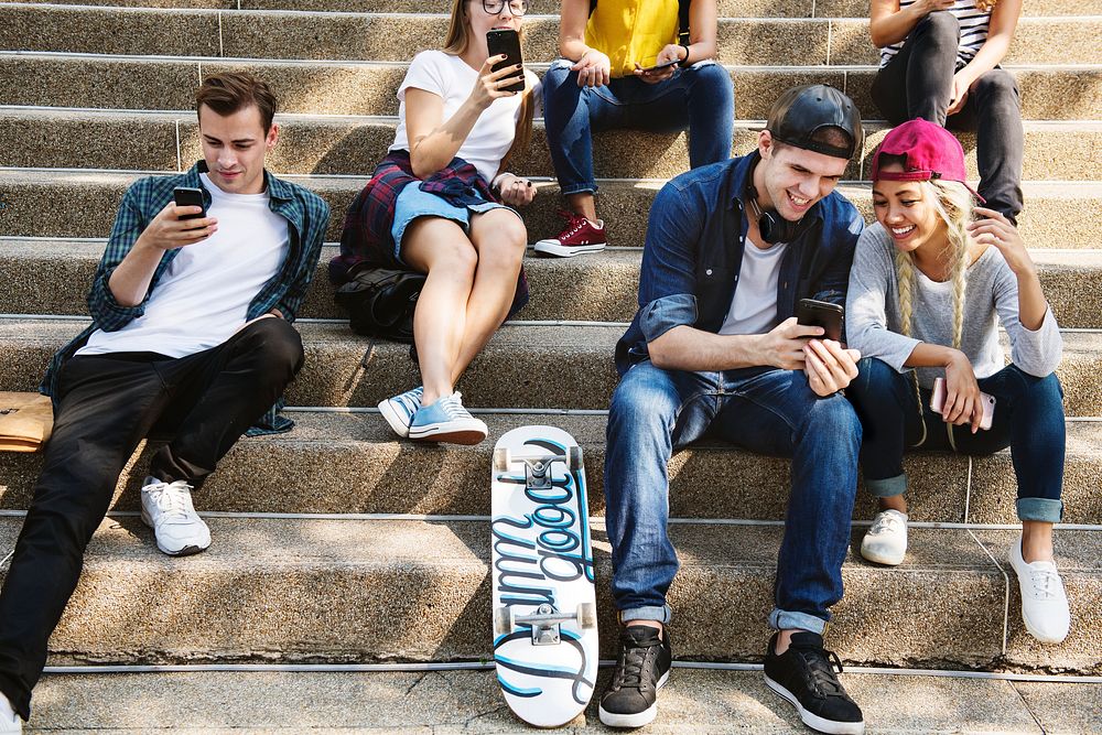 Friends sitting on the staircase using smartphones together and chilling