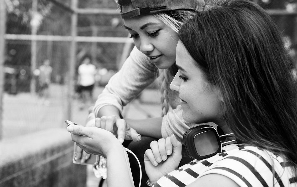 Young adult female friends listening to music through their smartphone outdoors