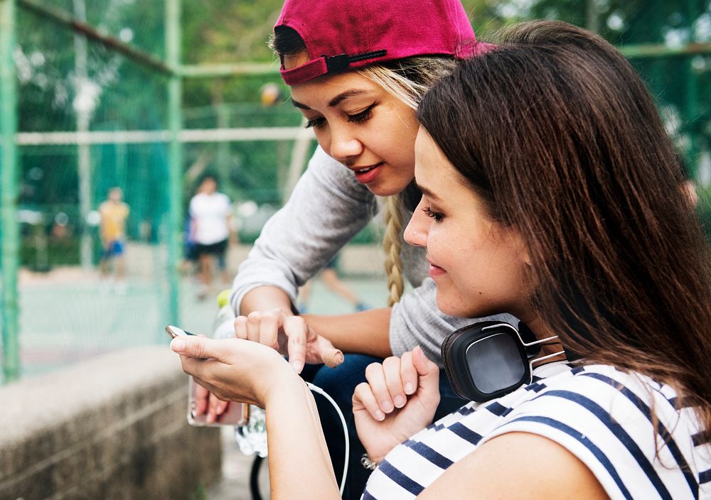 Young adult female friends listening to music through their smartphone outdoors