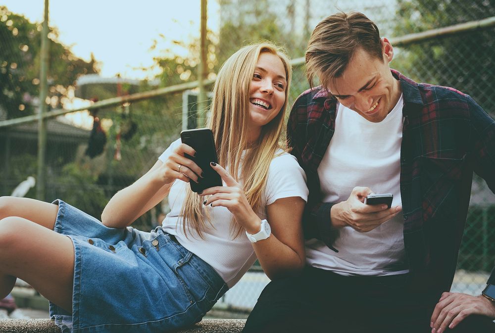 Happy cute young couple in the park using smartphones together