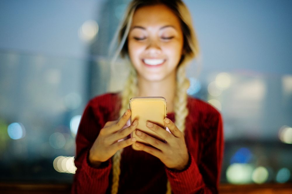 Smiling young woman using a smartphone in the evening cityscape