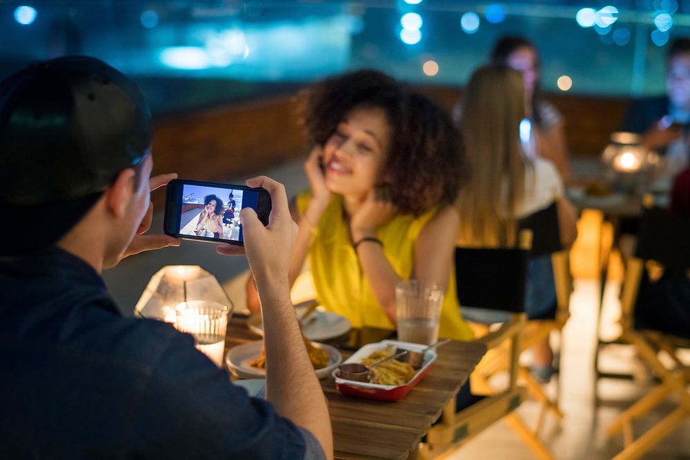 Young adult couple on a dinner date taking smartphone photos