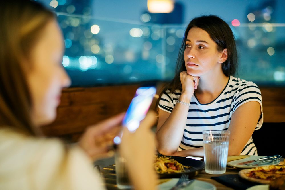 Young woman being bothered by a friend using a smartphone smartphone addiction and social issue concept