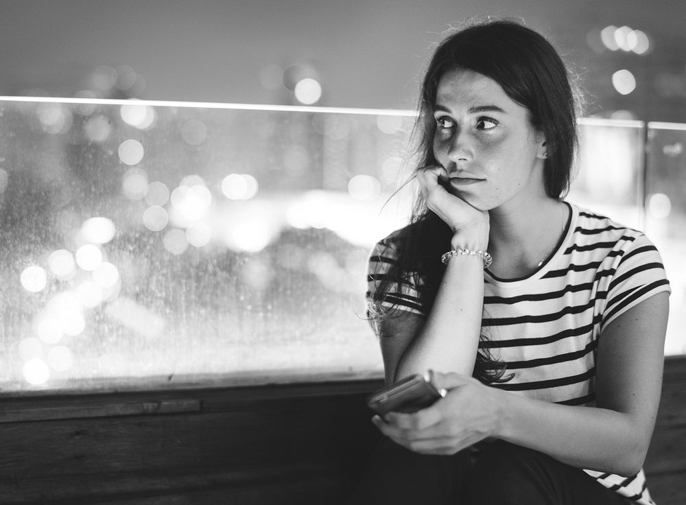 Unhappy young woman holding a smartphone in the evening cityscape