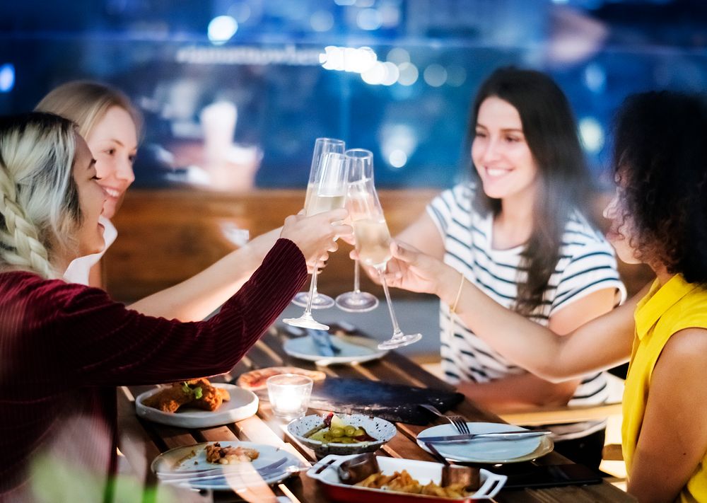 Girl friends toasting at dinner together at a rooftop bar