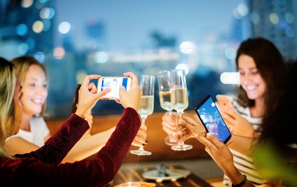 Girl friends having a dinner together at a rooftop bar taking a photo of the toast social media concept