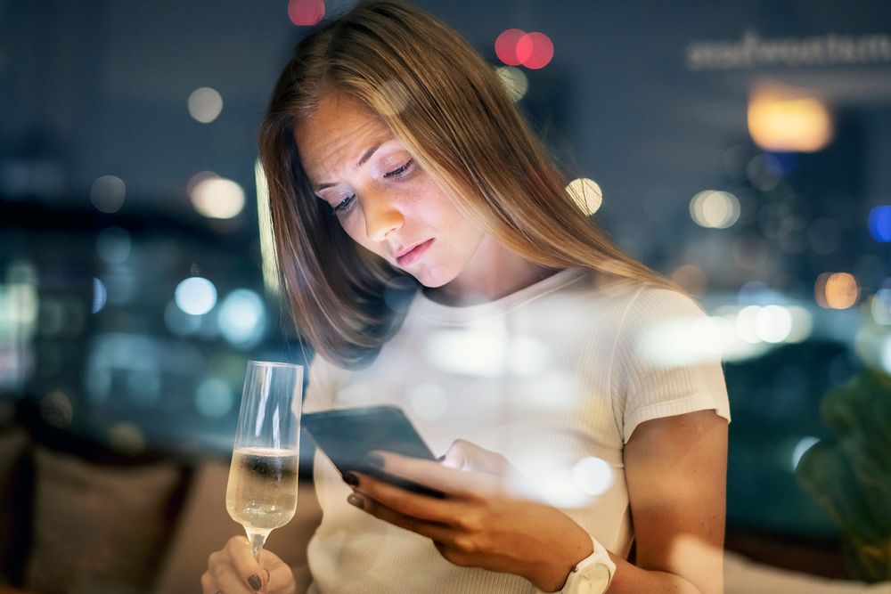 Serious young woman using a smartphone at a rooftop bar in the evening