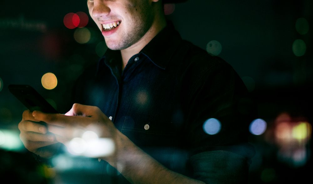 Happy young adult male using a smartphone in a night cityscape