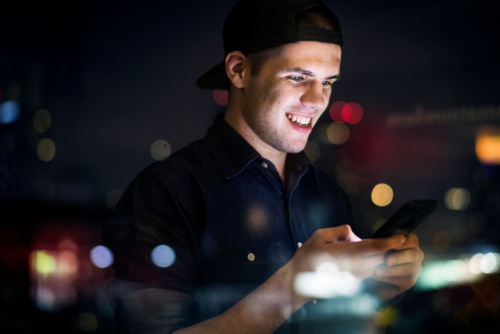 Happy young adult male using a smartphone in a night cityscape