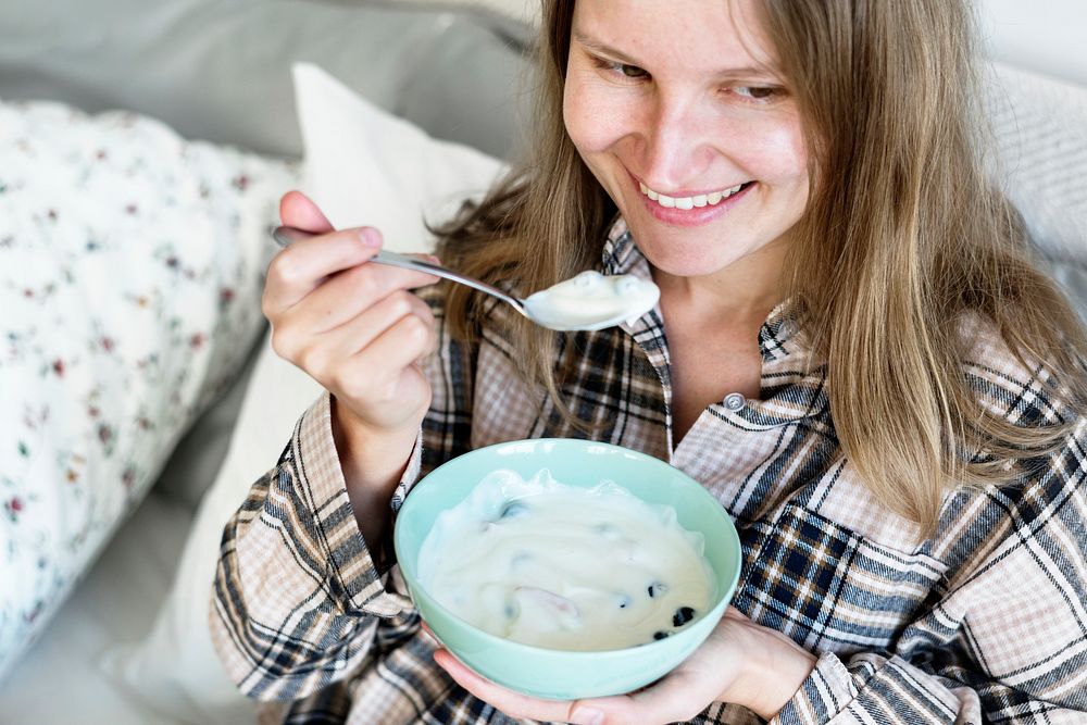 Caucasian girl eating yogurt on bed