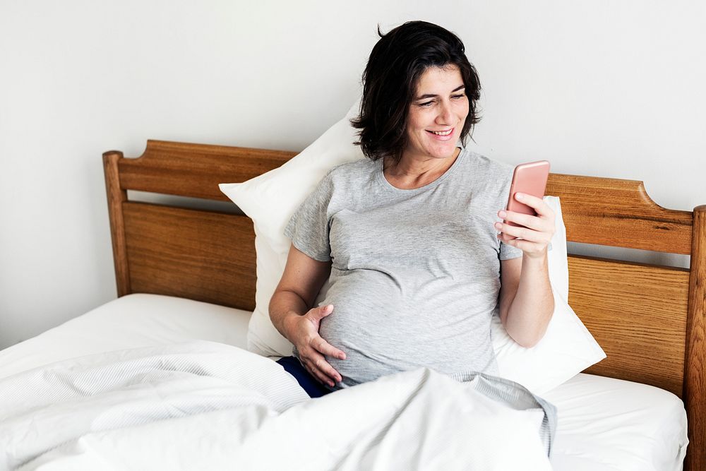 Pregnant woman using a mobile phone on the bed