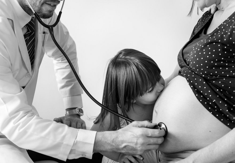 Daughter kissing pregnant mother's belly while having a fetal monitoring