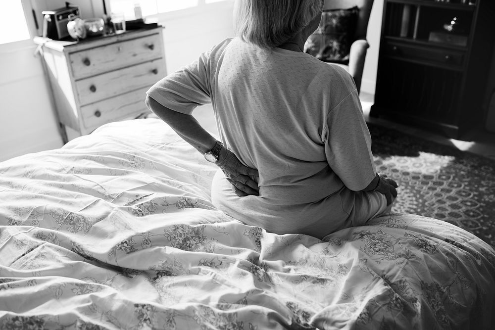 Black and white photo of a senior woman sitting on the bed in pain