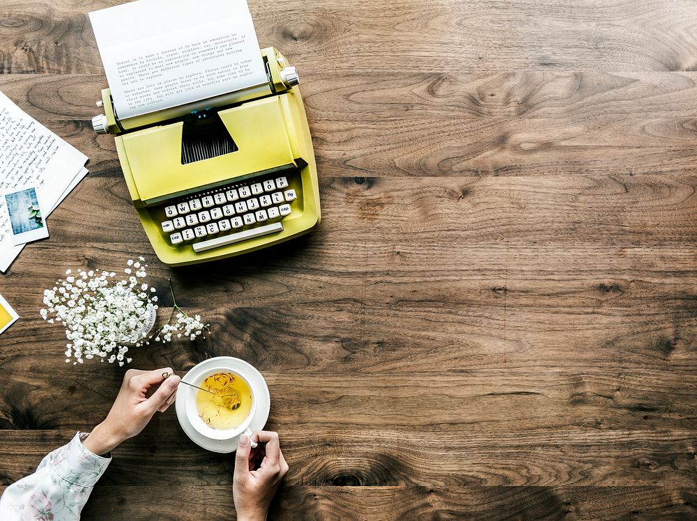 Aerial view of retro typewriter and a woman with a cup of tea