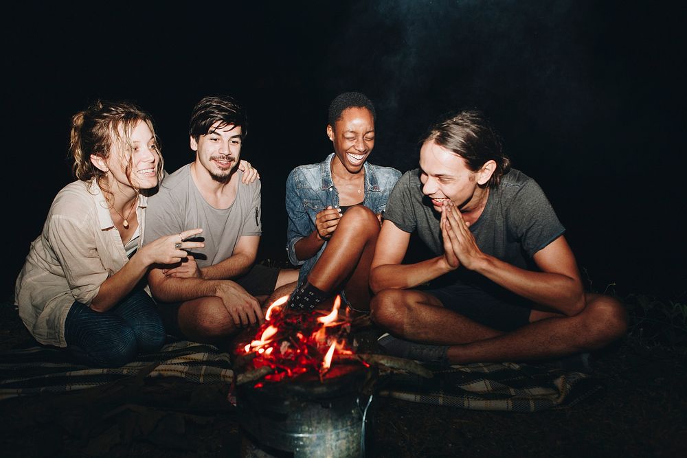 Group of young adult friends sitting around the bonfire outdoors recreational leisure and friendship concept