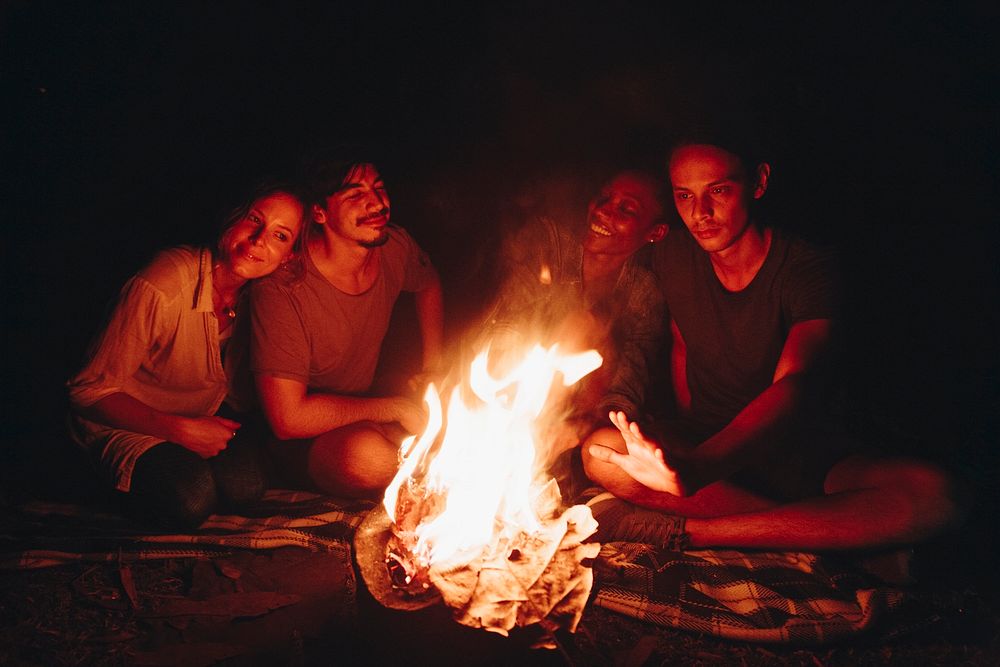 Group of young adult friends sitting around the bonfire outdoors recreational leisure and friendship concept
