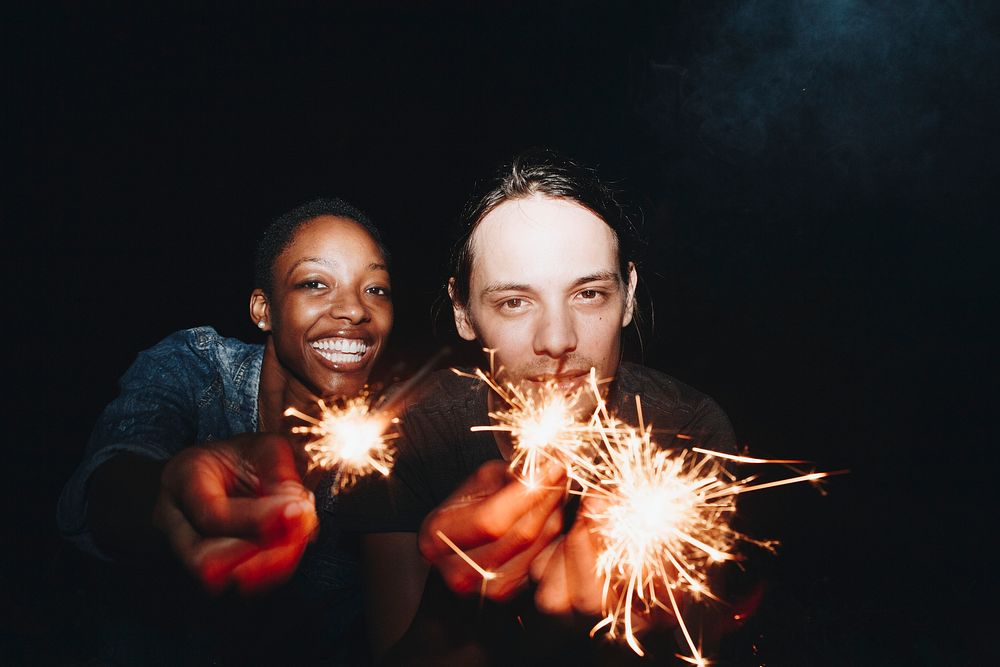 African American woman and a Caucasian man couple playing with sparklers celebration and festive party concept