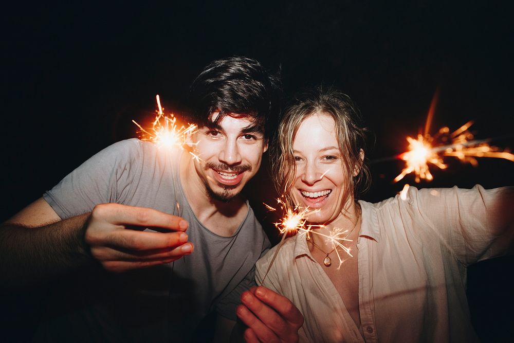 Caucasian man and woman couple playing with sparklers celebration and festive party concept