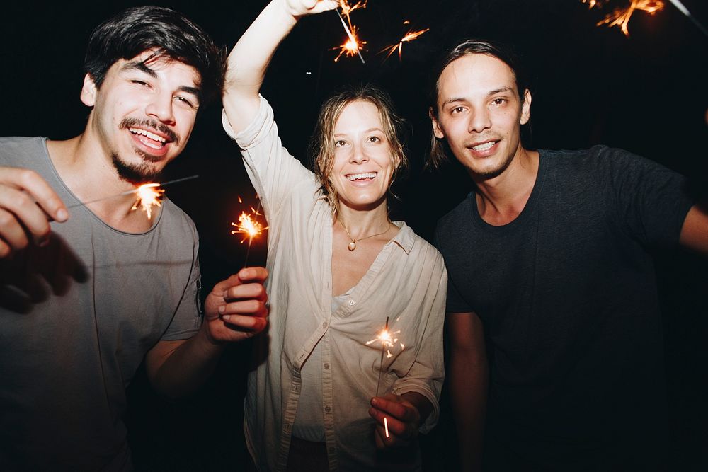 Two Caucasian men and a woman playing with sparklers celebration and festive party concept