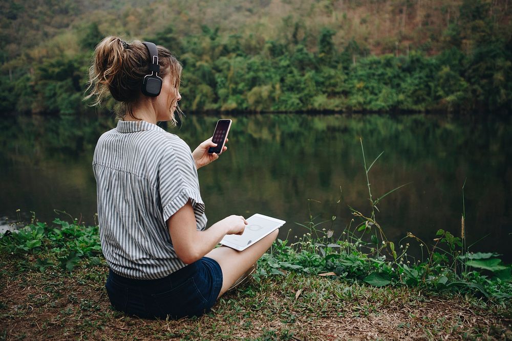 Woman alone in nature listening to music with headphones, digital tablet and a smartphone music and relaxation concept