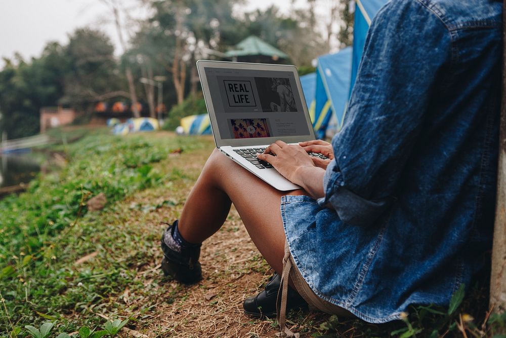 Woman alone in nature using a laptop on a camp site getaway from work or internet addiction concept