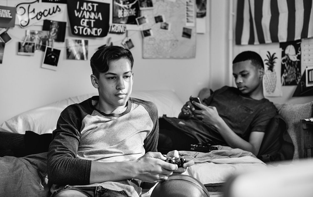 Teenage boys hanging out in a bedroom playing a video game and using a smartphone