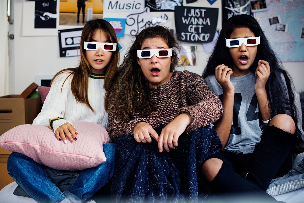 Teenage girls wearing 3d movie eyeglasses surprised scared and watching TV