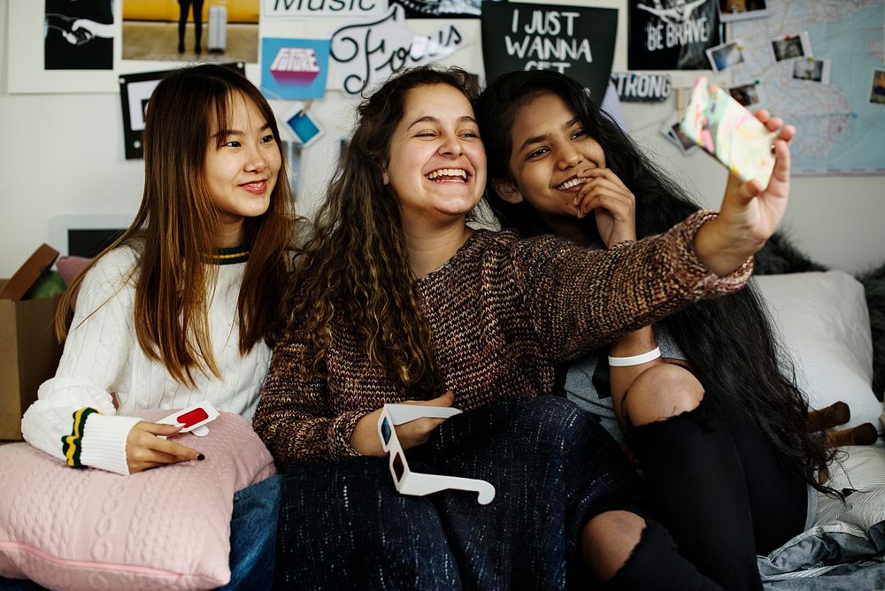Teenage girls using a smartphone to take a selfie in a bedroom hangout and friendship concept