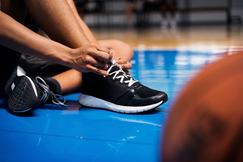 African American teenage boy tying his shoe laces on a basketball court