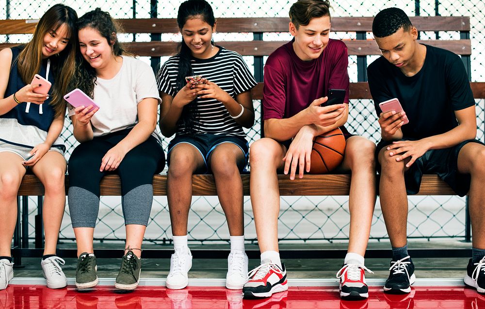 Group of young teenager friends on a basketball court relaxing using smartphone