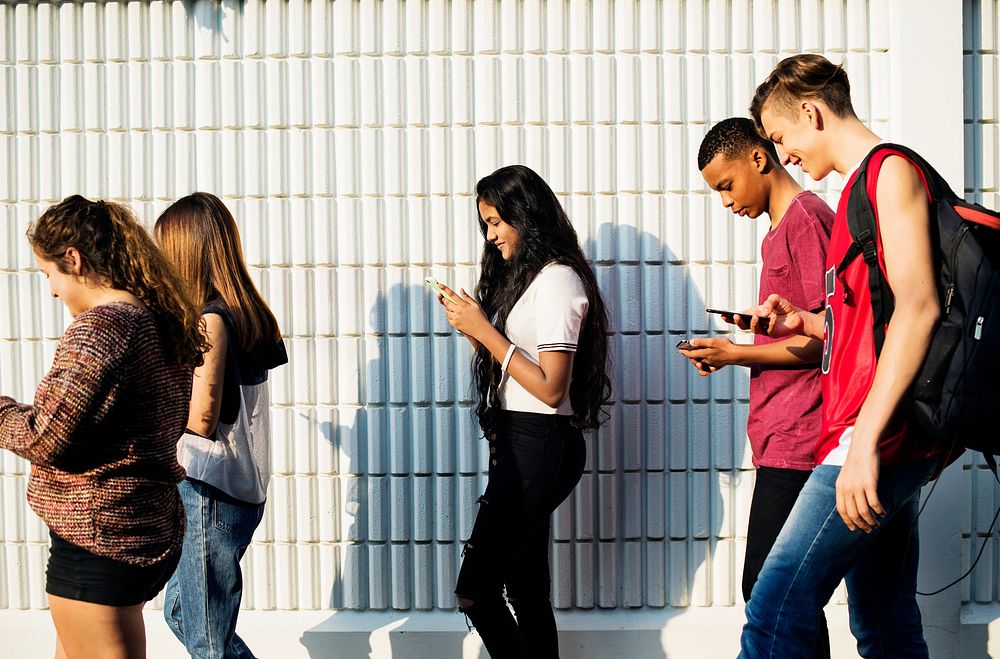 Group of diverse teenagers using phones while walking
