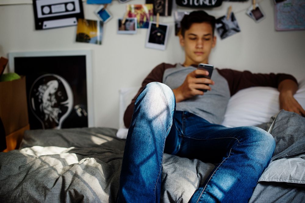 Teenage boy using smartphone in a bedroom social media concept