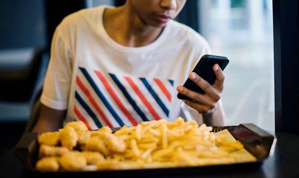 Close up of teenage boy using a smartphone eating french fries youth culture concept