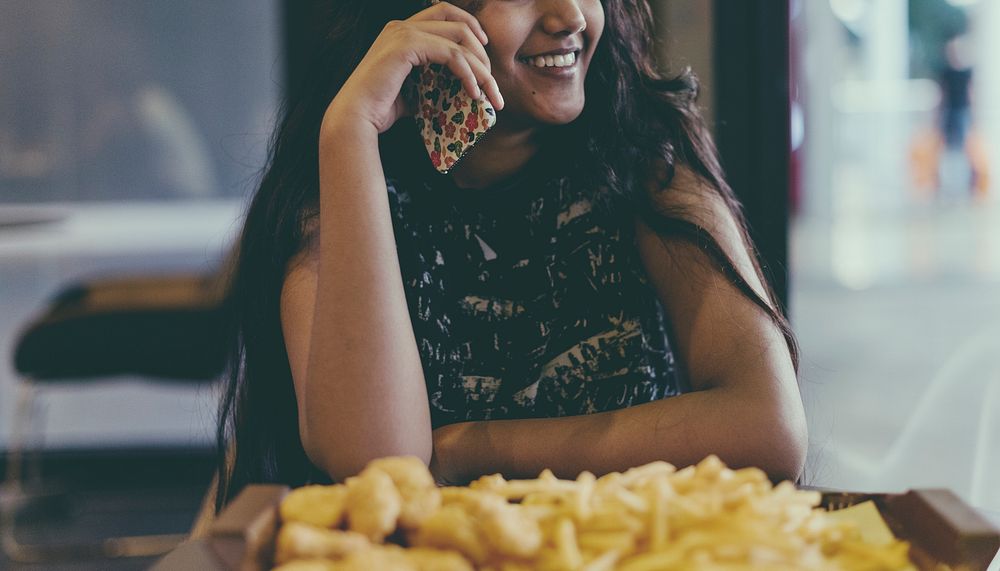 Close up of teenage girl talking on a phone eating french fries youth culture concept