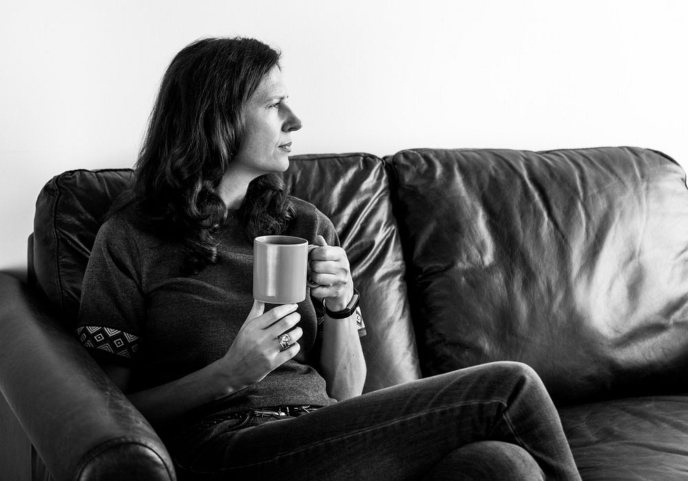 Thoughtful woman drinking tea or coffee sitting on a cozy couch